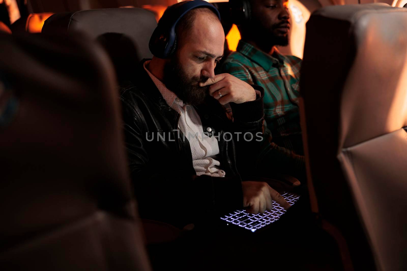 Young entrepreneur working on laptop and flying on business trip with airplane in economy class. International commercial flight with airline service, using computer during sunset.