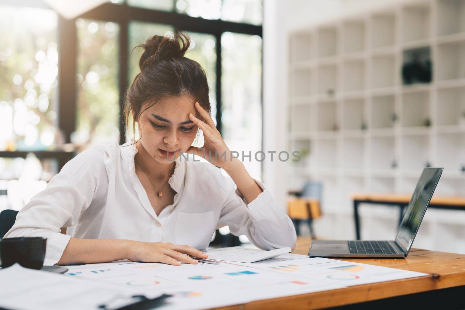 Young asian Woman Office Worker Uses Laptop, Feels Sudden Burst of Pain, Headache, Migraine. Overworked Accountant Feeling Project Pressure, Stress, Massages Her Head, Temples. by nateemee