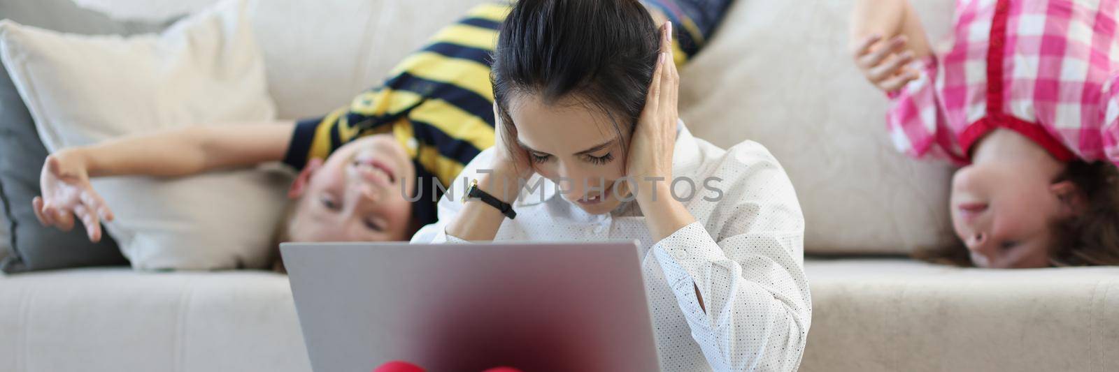 Low angle of lady try to concentrate on work while kids go nuts at home on quarantine. Woman with laptop close ears with hands. Remote job, babysit concept