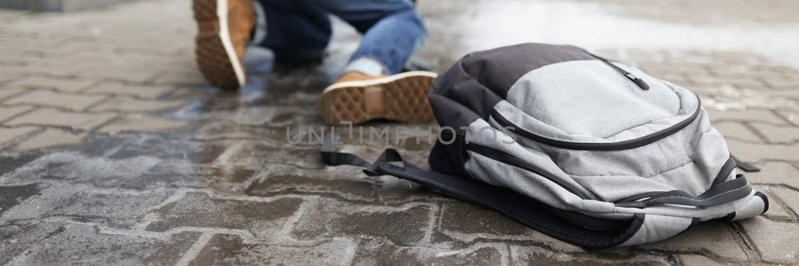 Low angle of man get up from ground after falling on slippery asphalt in winter. Backpack with personal things on surface. Injury, weather, trauma concept