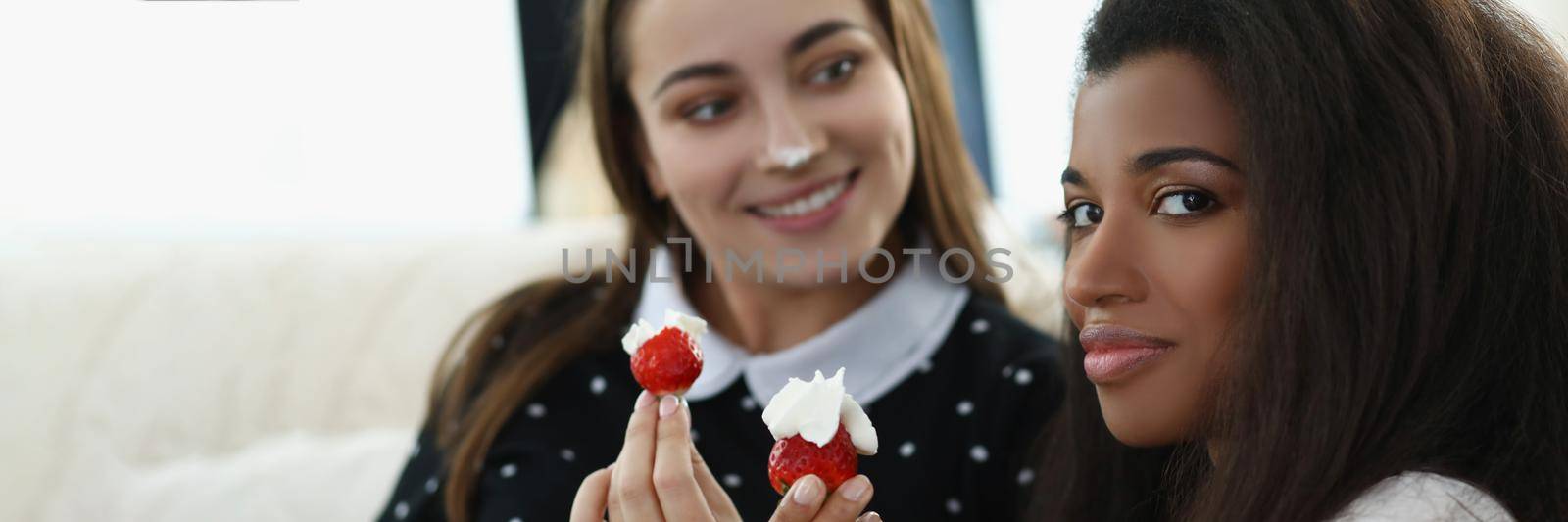 Portrait of smiling pretty women eating tasty fresh strawberry fruit covered with whipped cream. Romantic date at home, best friends. Lgbt, love concept