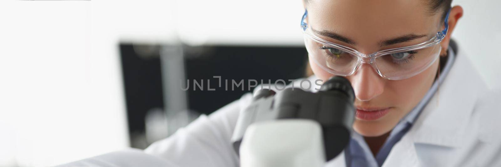 Portrait of female chemist investigate sample under microscope equipment in lab. Woman scientist explore material, protective uniform. Laboratory concept