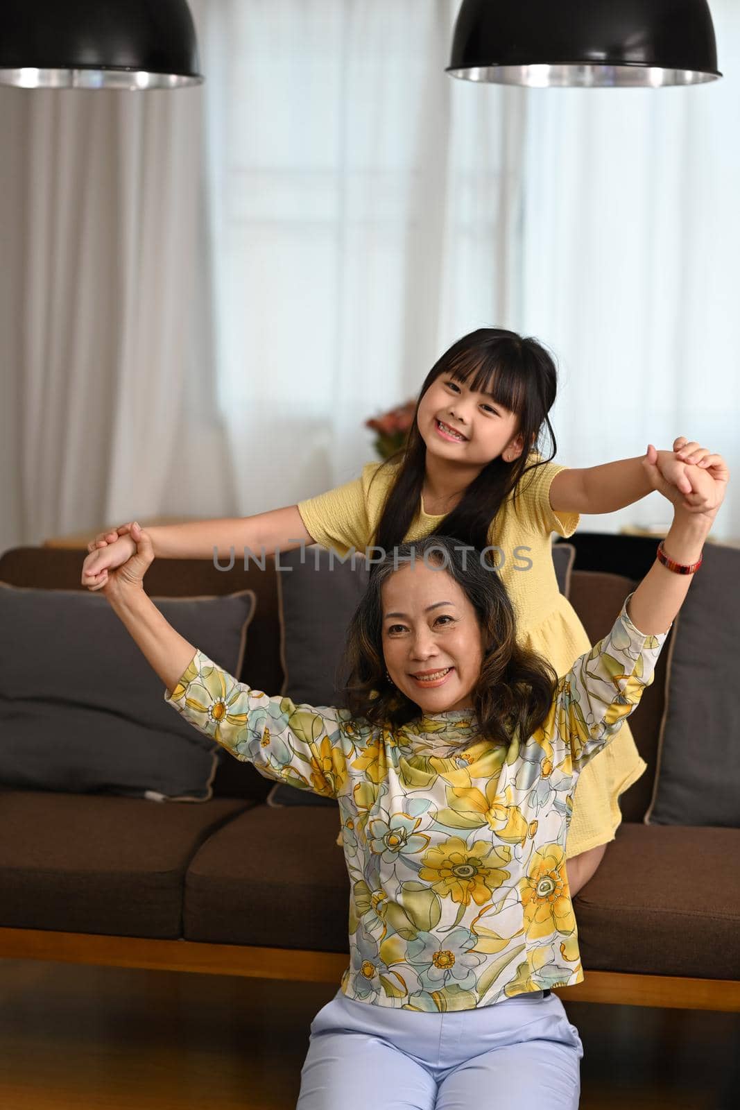 Happy middle aged grandmother and little child having fun spending leisure weekend at home together by prathanchorruangsak