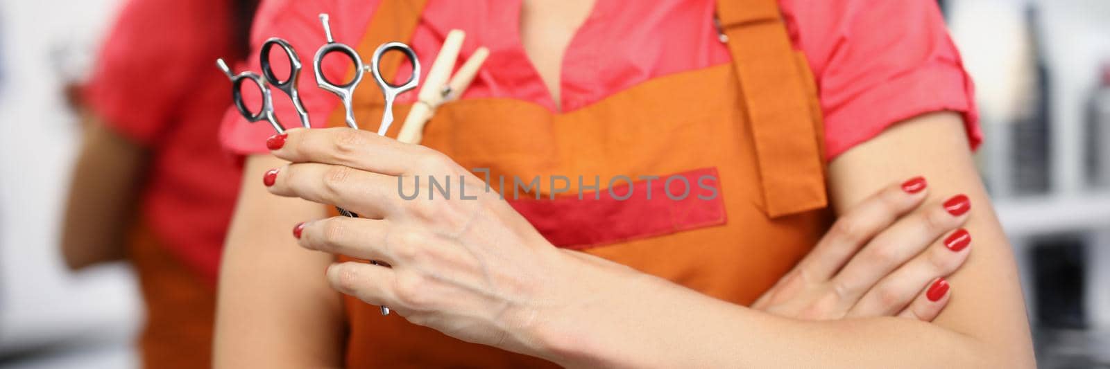 Close-up of young professional master holding equipment for work and posing in uniform. Qualified hairdresser hold pair of scissors. Beauty studio concept