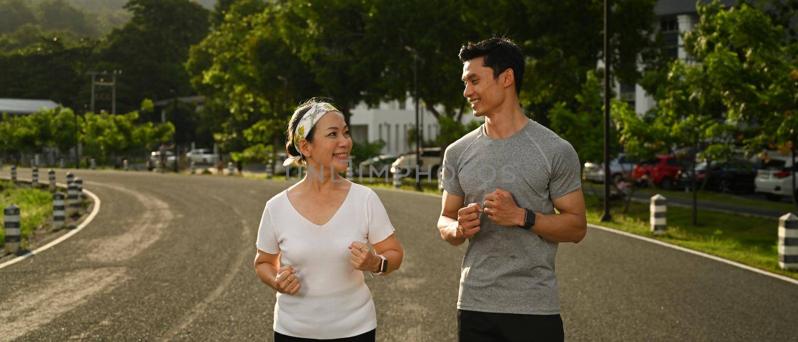 Energetic mature woman and young man jogging in the park. Fitness, sport and healthy lifestyle concept.
