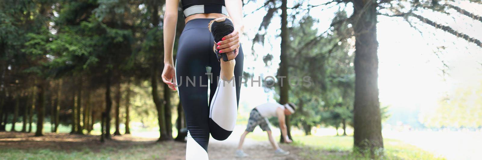 Low angle of young woman stand with back and stretching body before run. Active sportswoman in outfit for morning jogging. Active lifestyle, habit concept