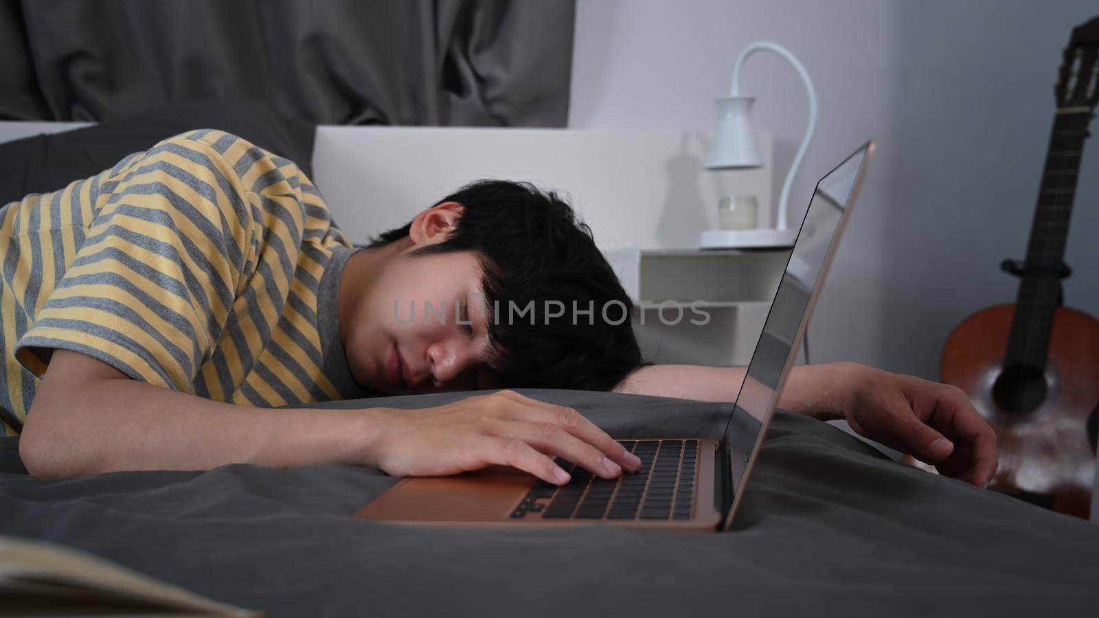 Tired young asian man sleeping on bed near computer laptop.