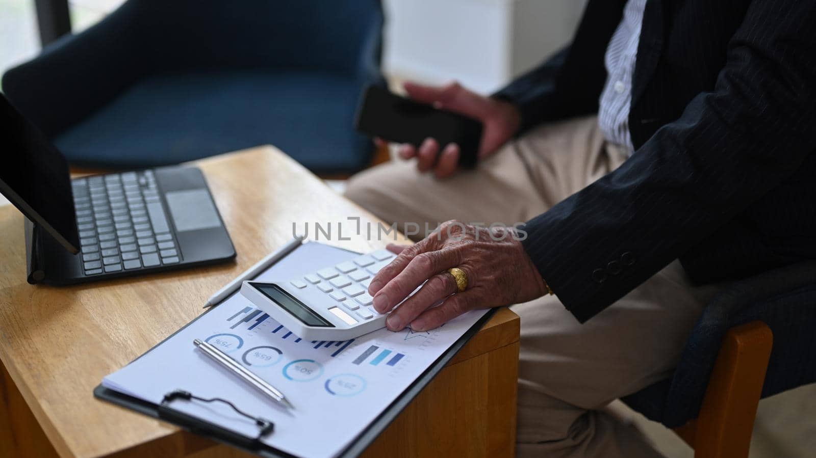 Cropped shot senior businessman holding mobile phone and using calculator in office. by prathanchorruangsak