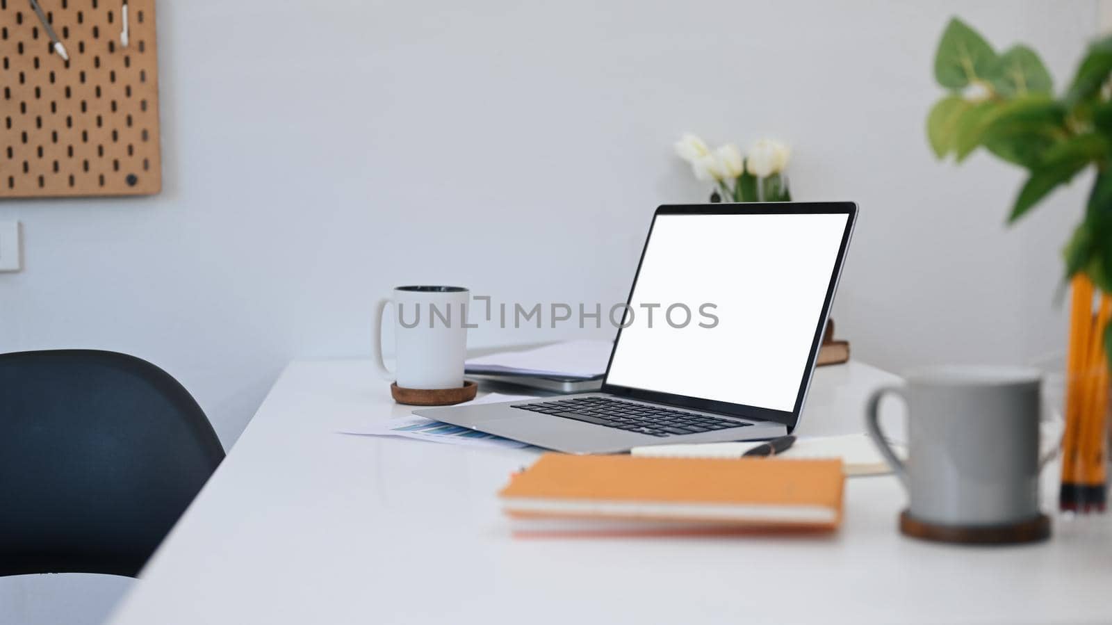 Computer laptop with blank screen, coffee cups, notebook and houseplant on white table by prathanchorruangsak