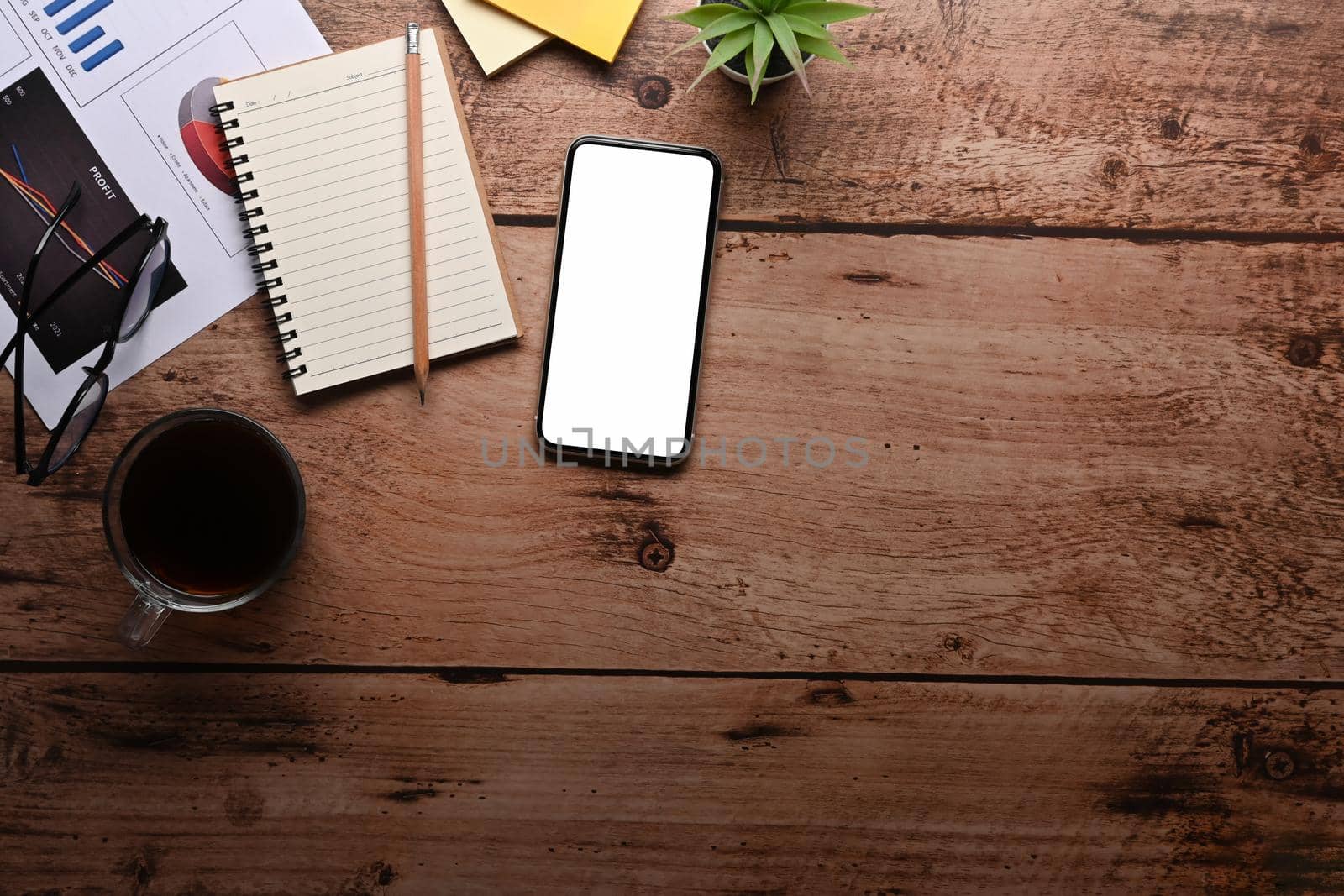Top view smart phone, notebook, coffee cup and financial documents on wooden table. by prathanchorruangsak