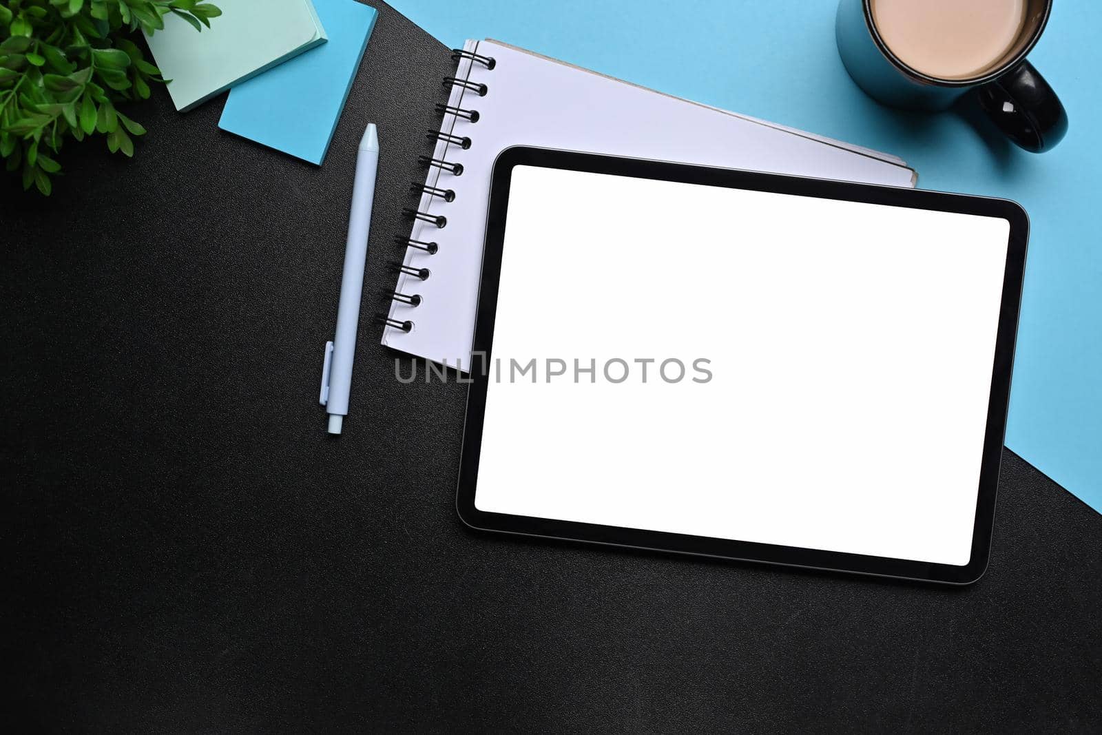 Digital tablet, notepad, sticky notes and coffee cup on black and blue background.
