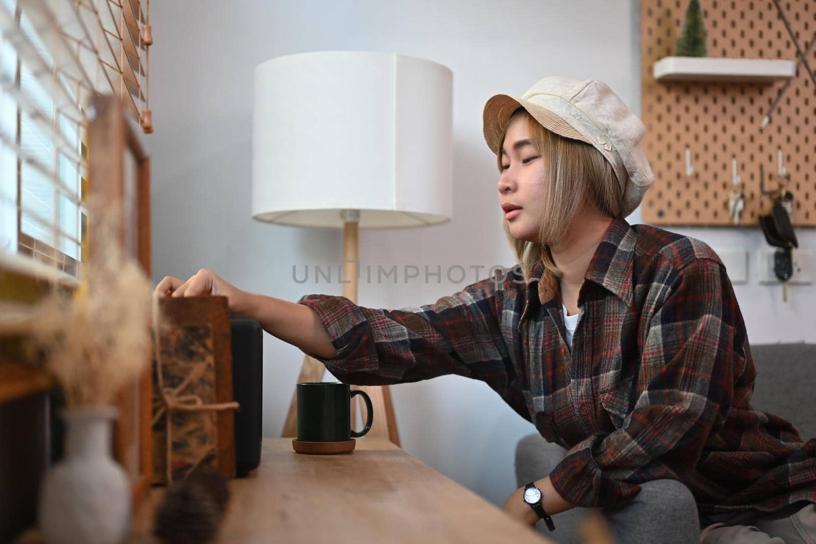 Smiling young woman turning on wireless speaker in living room. by prathanchorruangsak