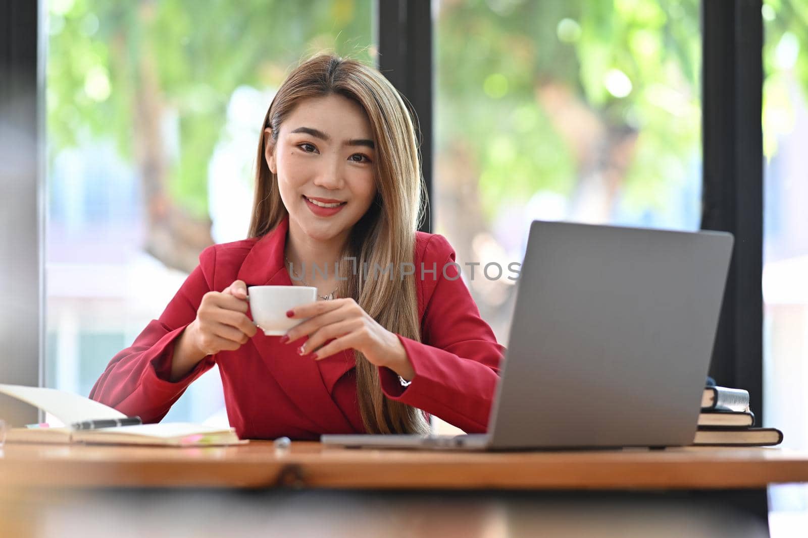Beautiful businesswoman sitting in front of computer laptop and drinking coffee in the morning. by prathanchorruangsak