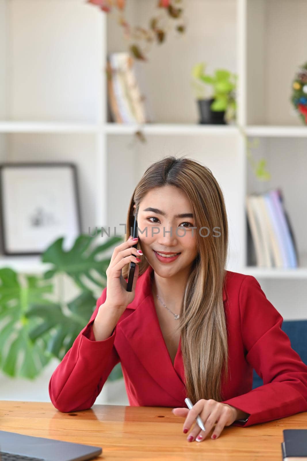 Portrait of attractive businesswoman sitting in office and talking on mobile phone. by prathanchorruangsak