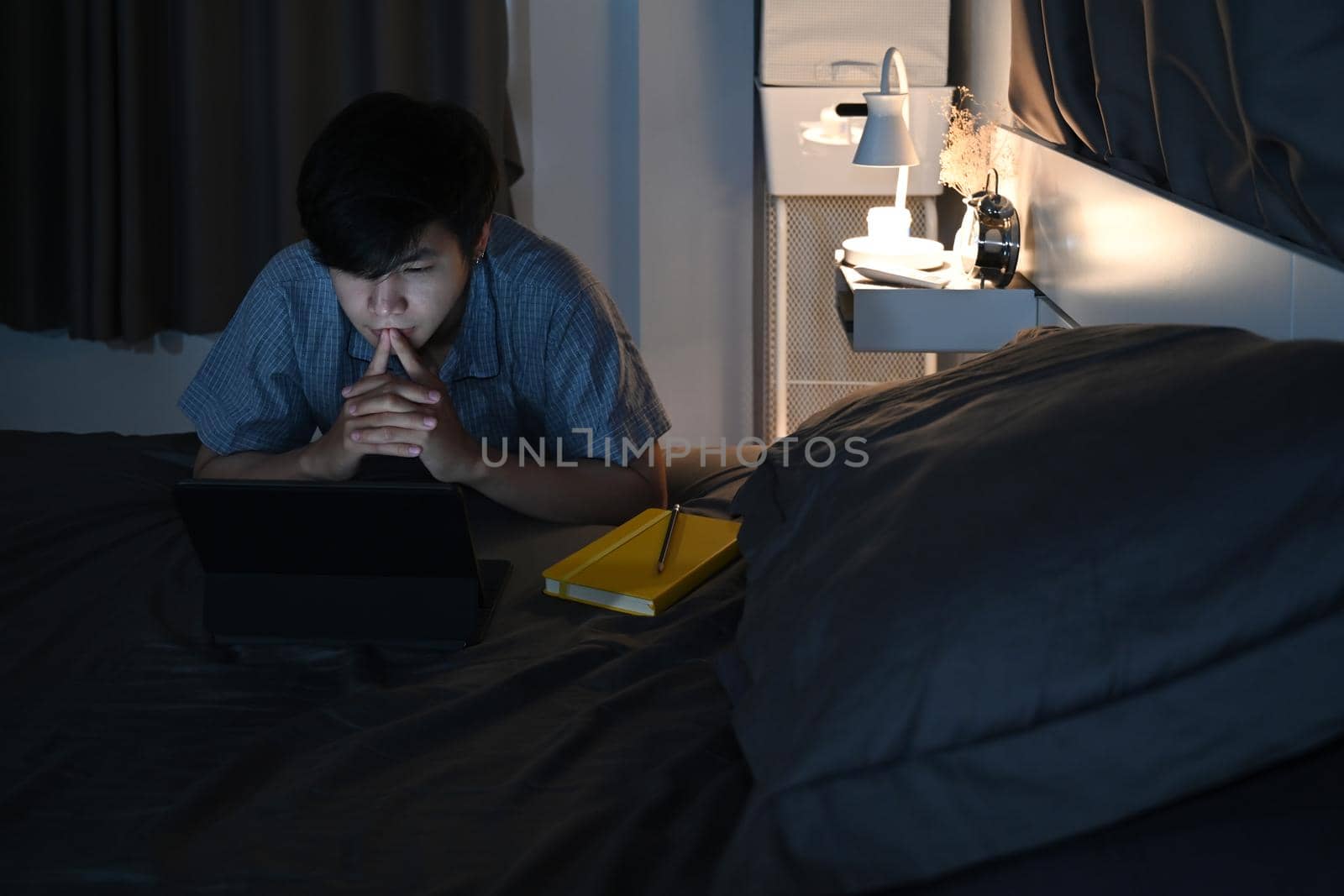 Man sitting in bedroom and using computer tablet at late night. by prathanchorruangsak