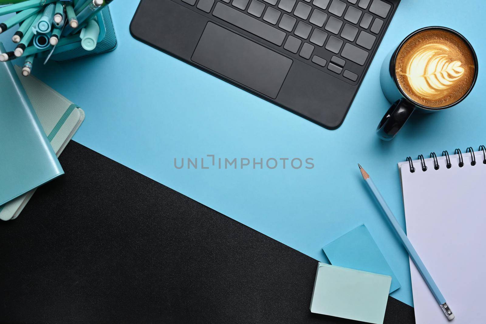 Creative workspace with computer tablet, coffee cup and notebook on blue background. by prathanchorruangsak