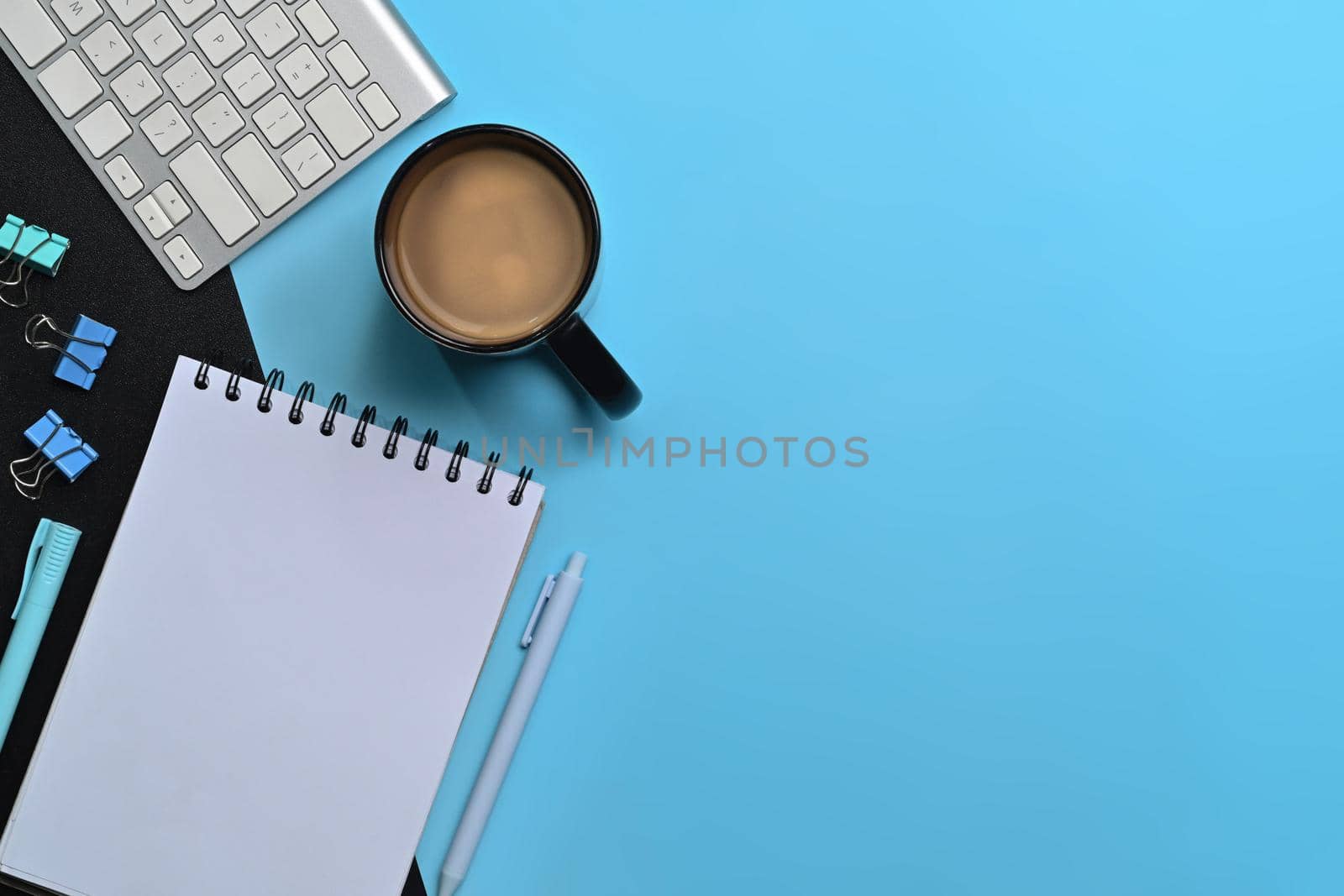 Flat lay empty notebook, coffee cup and keyboard on blue background. by prathanchorruangsak