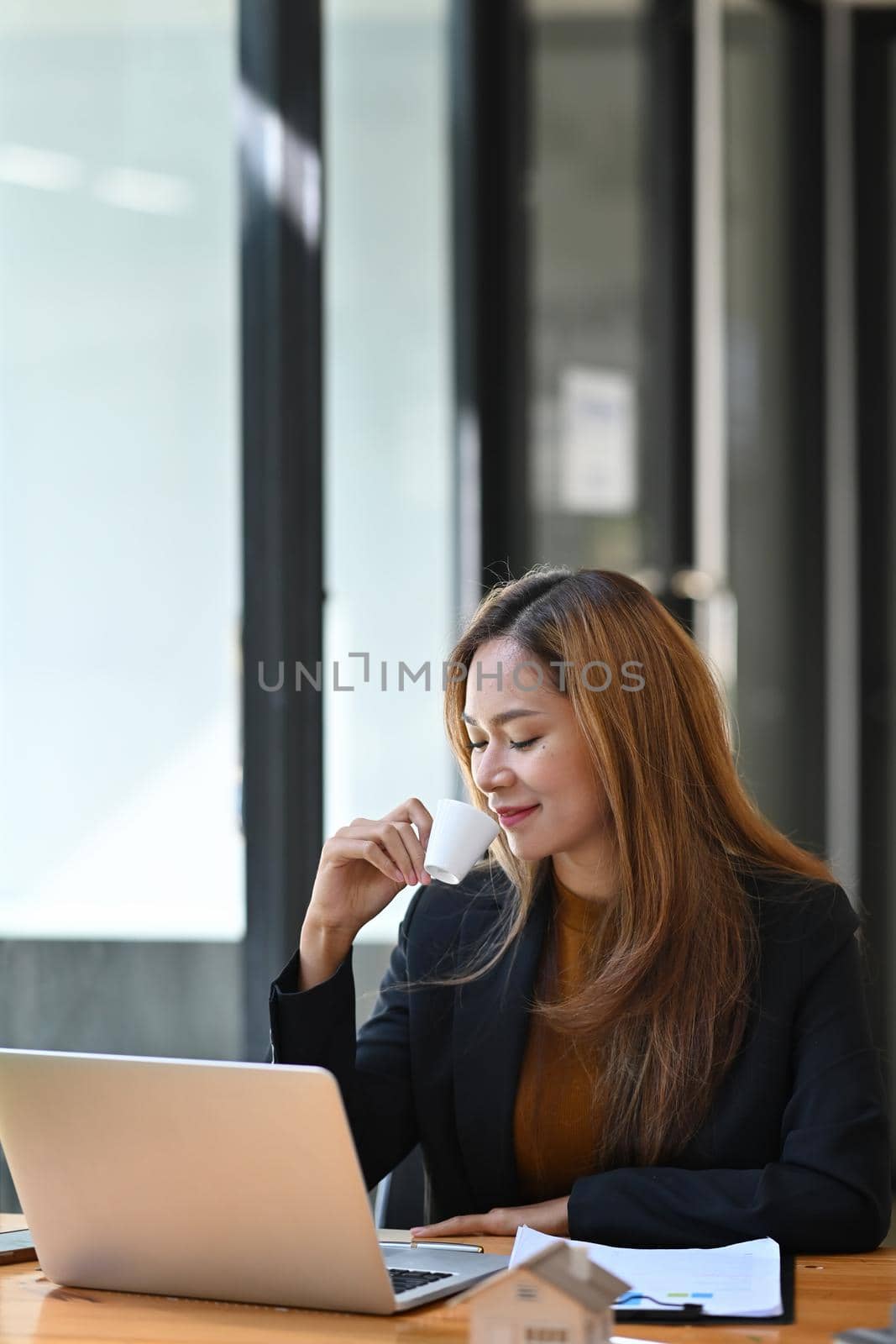 Positive businesswoman sitting at her workplace and drinking coffee. by prathanchorruangsak