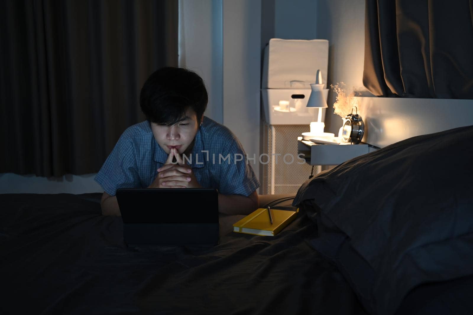 Young asian man watching movies on digital tablet at night.