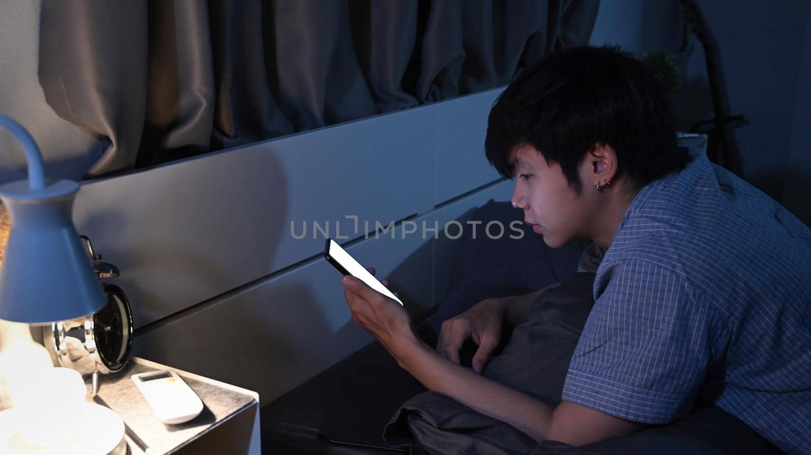 Man lying on comfortable bed and using smart phone at late night. by prathanchorruangsak