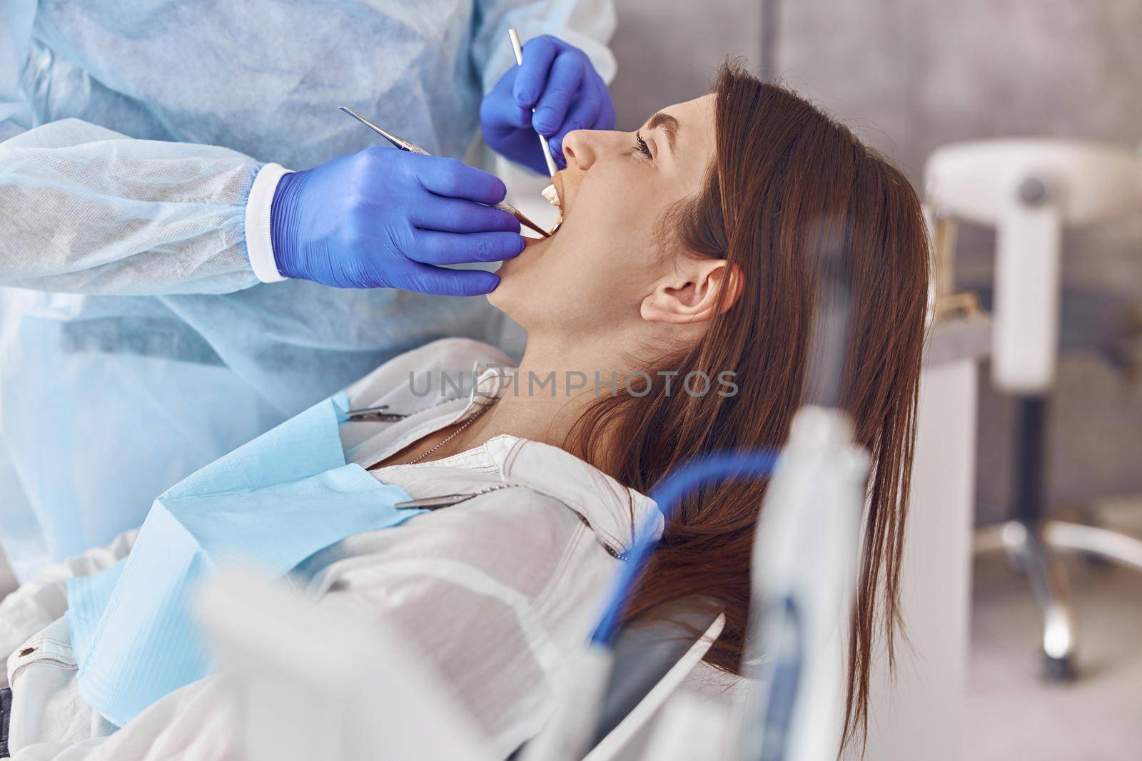 Professional doctor is doing tooth surgery to happy caucasian woman in modern dental cabinet