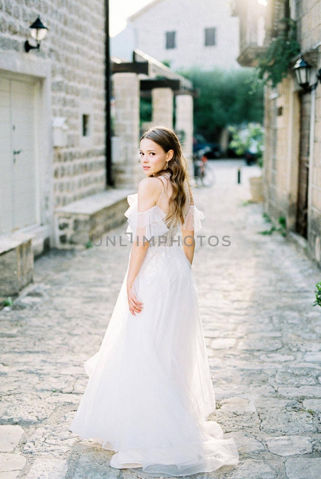 Bride stands half-turned on a cobbled narrow street of an old town. High quality photo