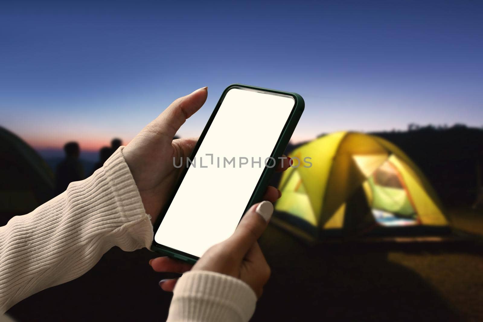 Young woman using smart phone near camping tent in the evening.