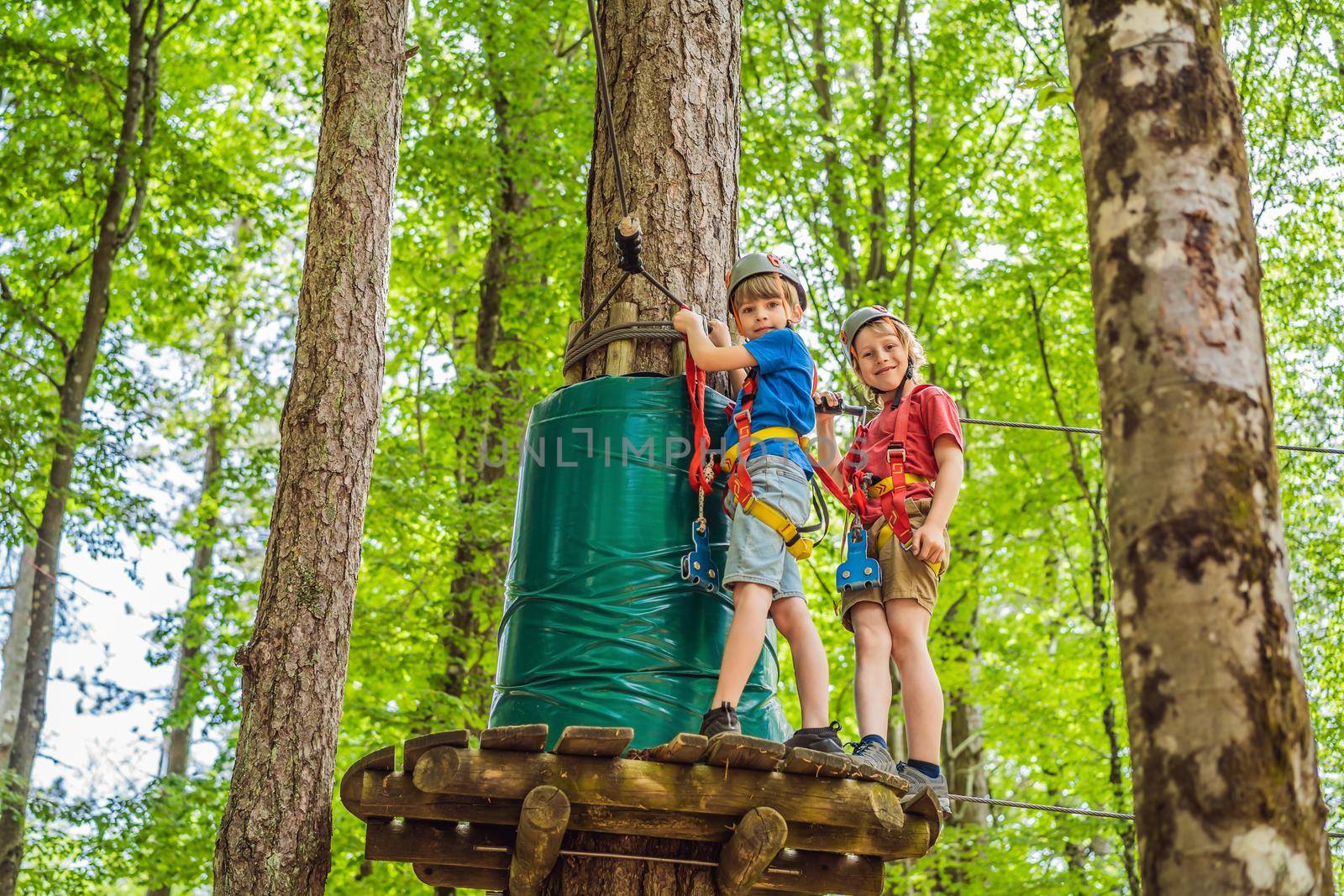 Two boys in a helmet, healthy teenager school boy enjoying activity in a climbing adventure park on a summer day.