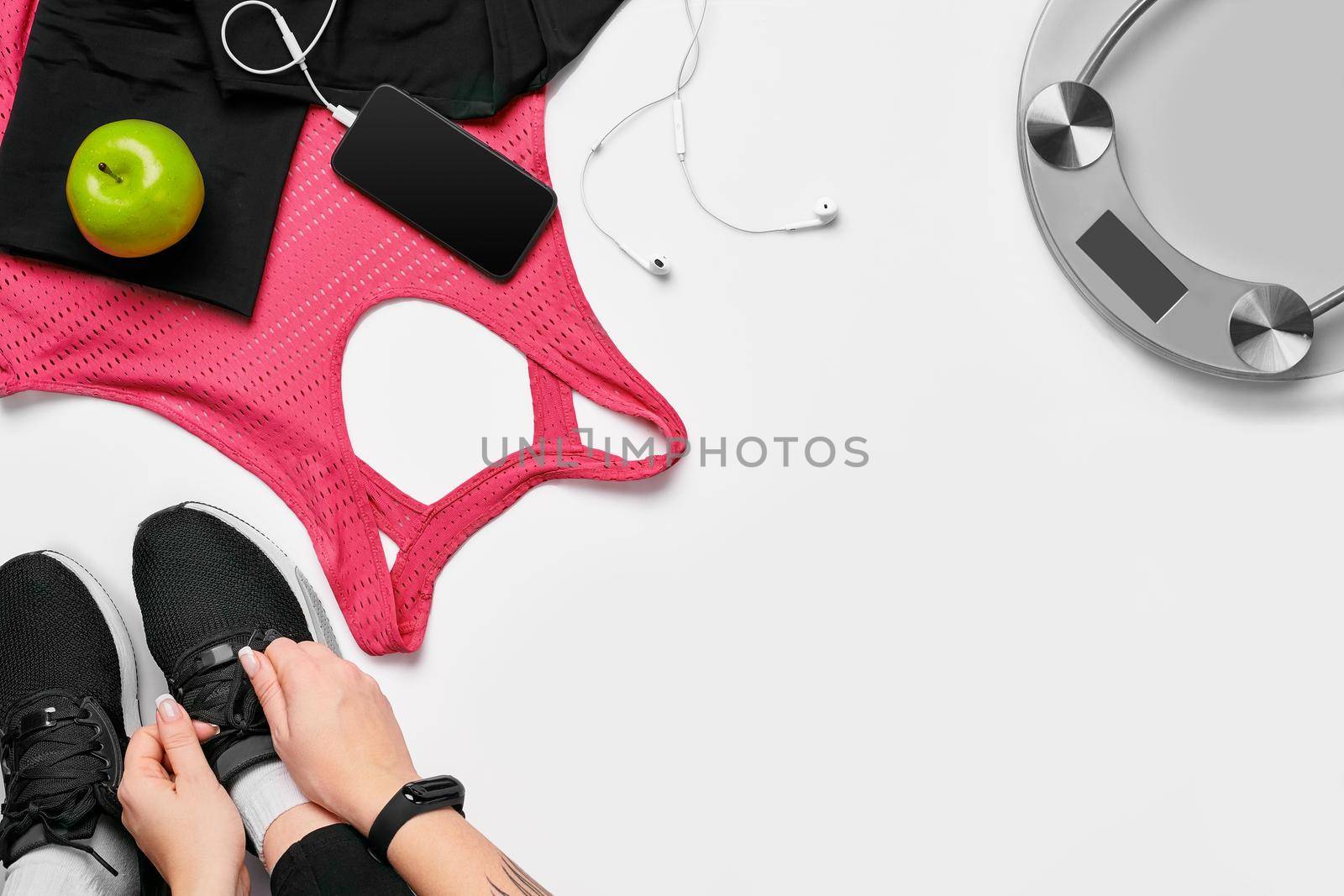 Overhead view of woman hands tying shoes with sport equipments on white background. Top view. Still life. Sports shoes, Fitness concept