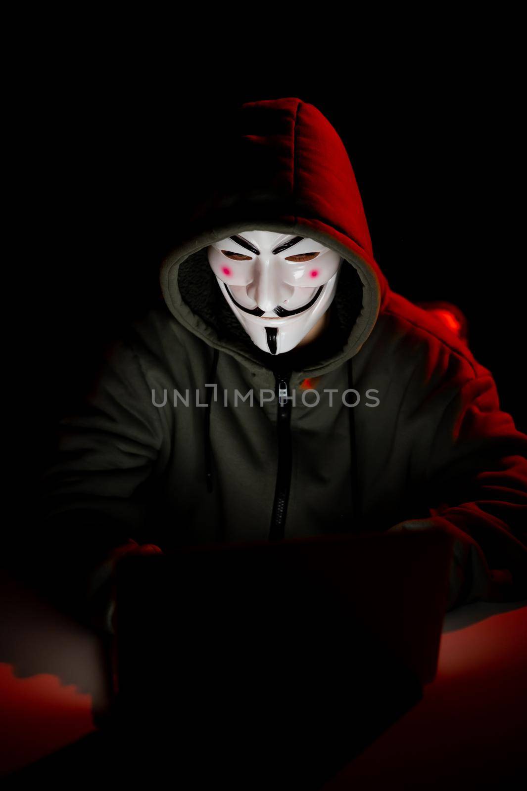 June 5, 2022 Novosibirsk, Russia: Anonymous in a hood is typing on a laptop in the dark in red light