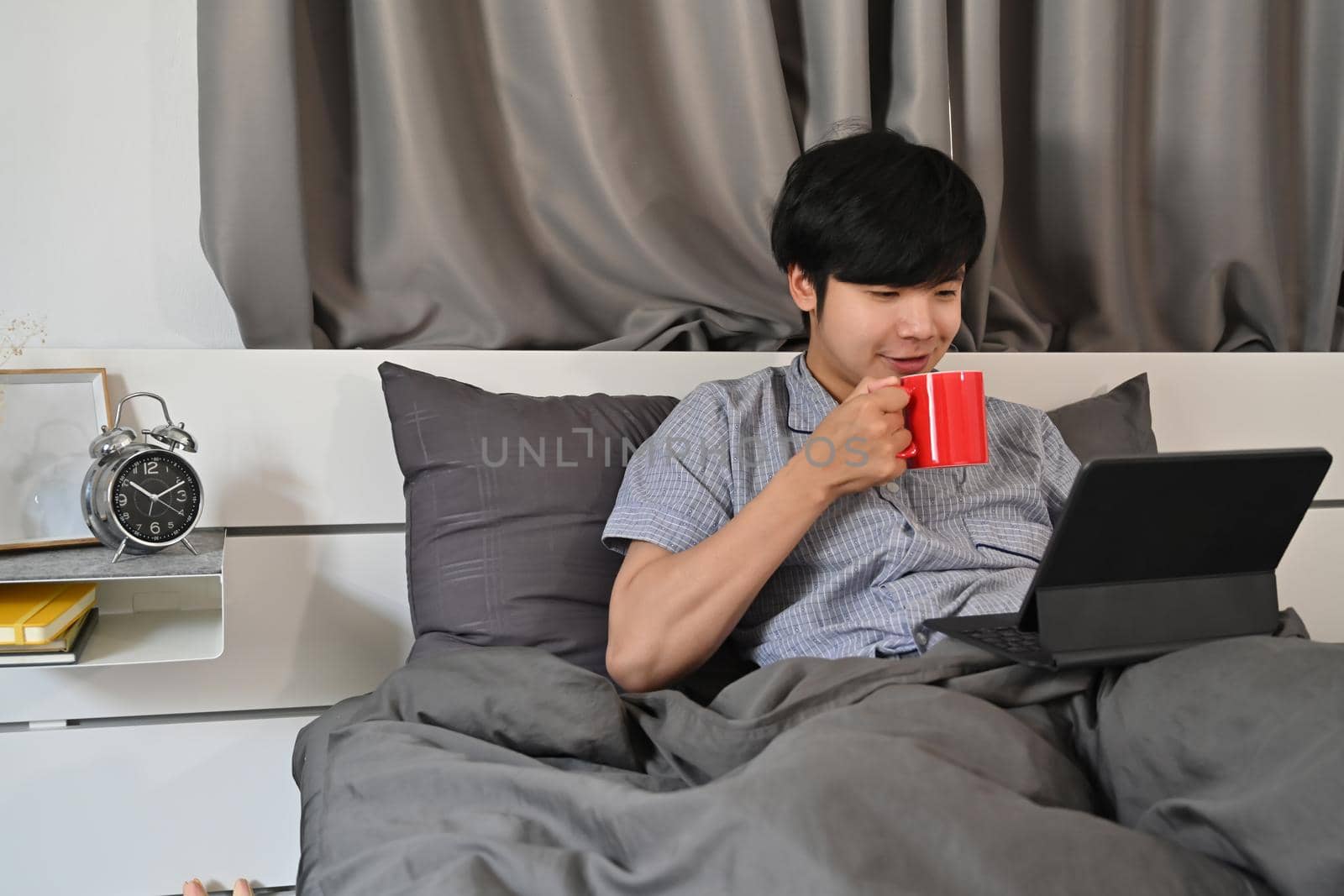 Young man drinking coffee and surfing internet with digital tablet in the morning. by prathanchorruangsak