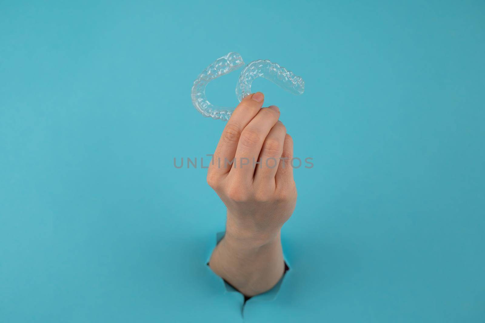 A female hand sticking out of a hole from a blue background holds removable night retainers