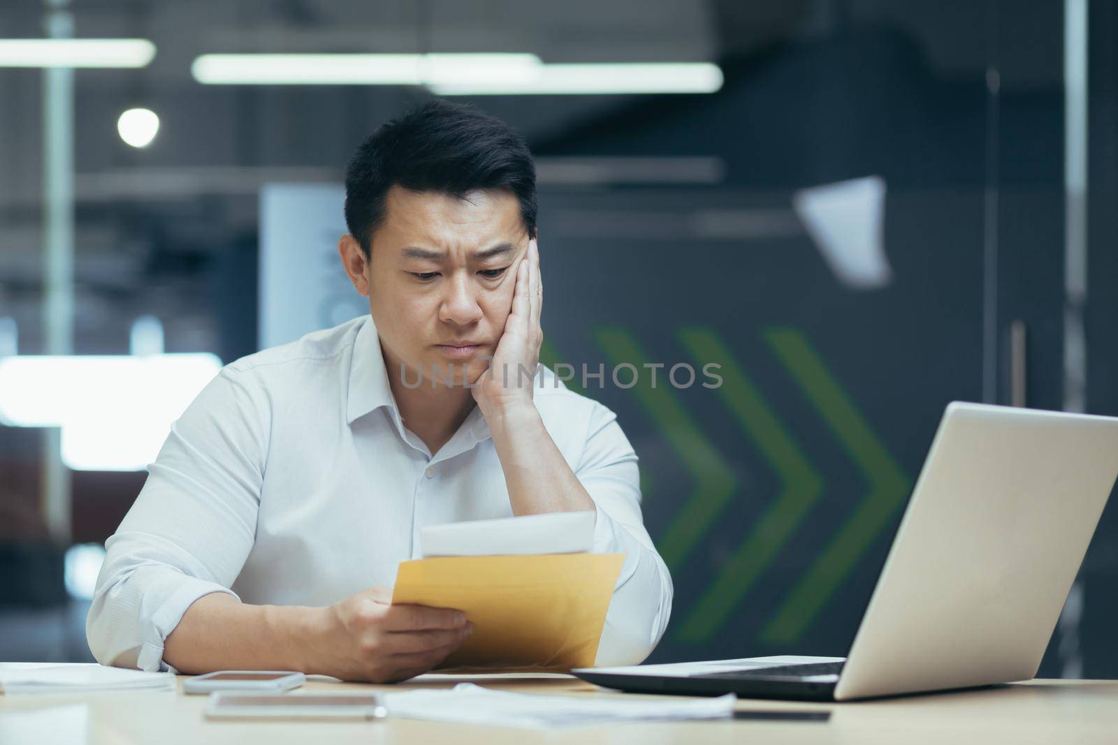 Sad over thinking asian businessman reading bad news letter from bank, male boss in shirt working in office
