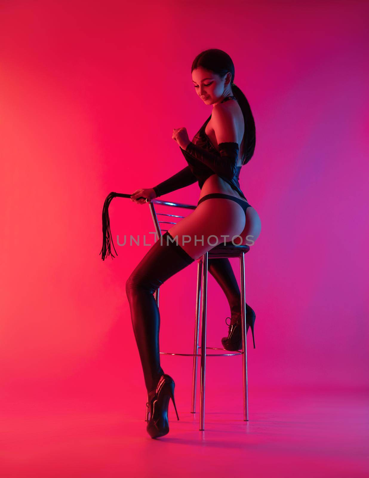 the sexy girl with beautiful buttocks in latex bdsm dress in neon light