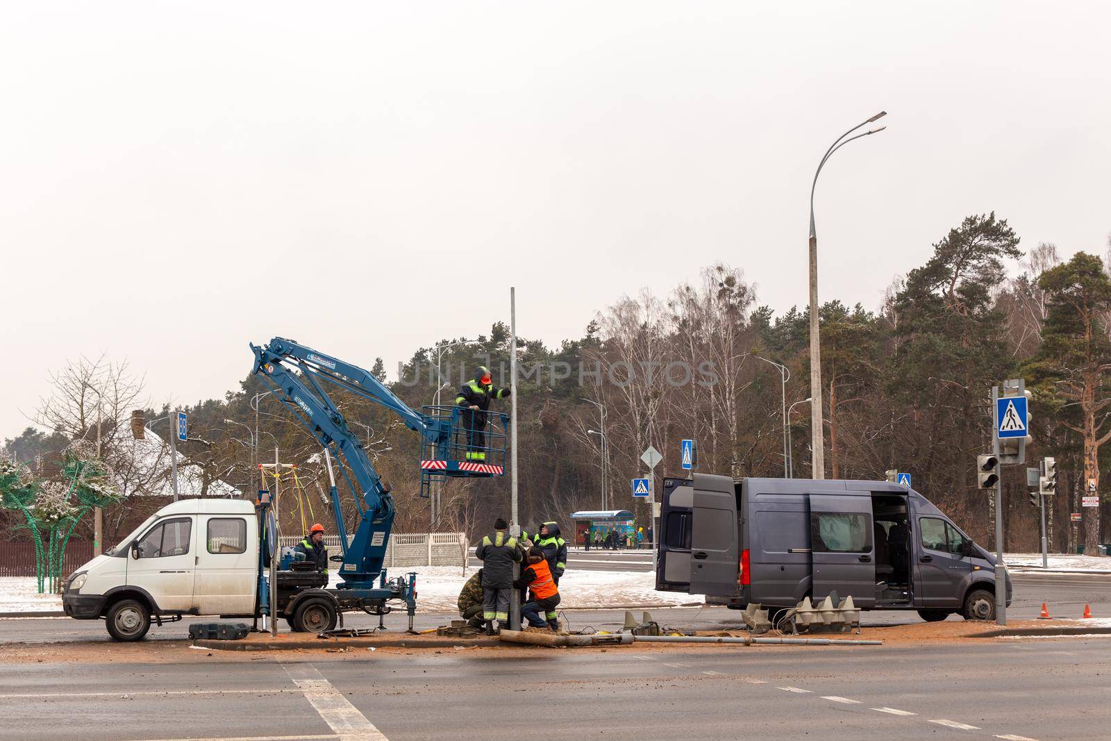 Grodno, Belarus - December 23, 2021: A team of workers is repairing a traffic light that was broken as a result of a traffic accident. Workers use a car-based lift.