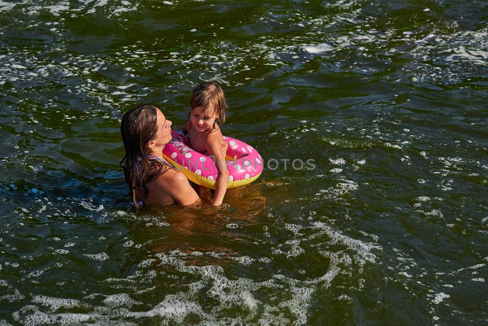 Cute girl on a swimming circle bathes with her mother protecting her in the sea by jovani68