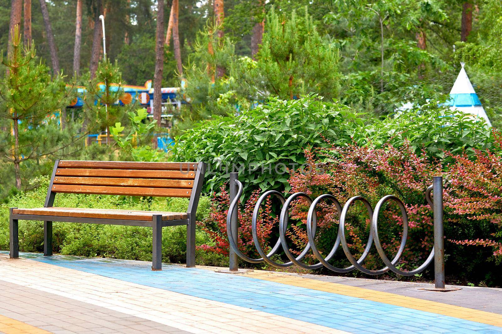 a large public green area in a town, used for recreation. Wooden bench and bike rack in a green city park with rides and trees