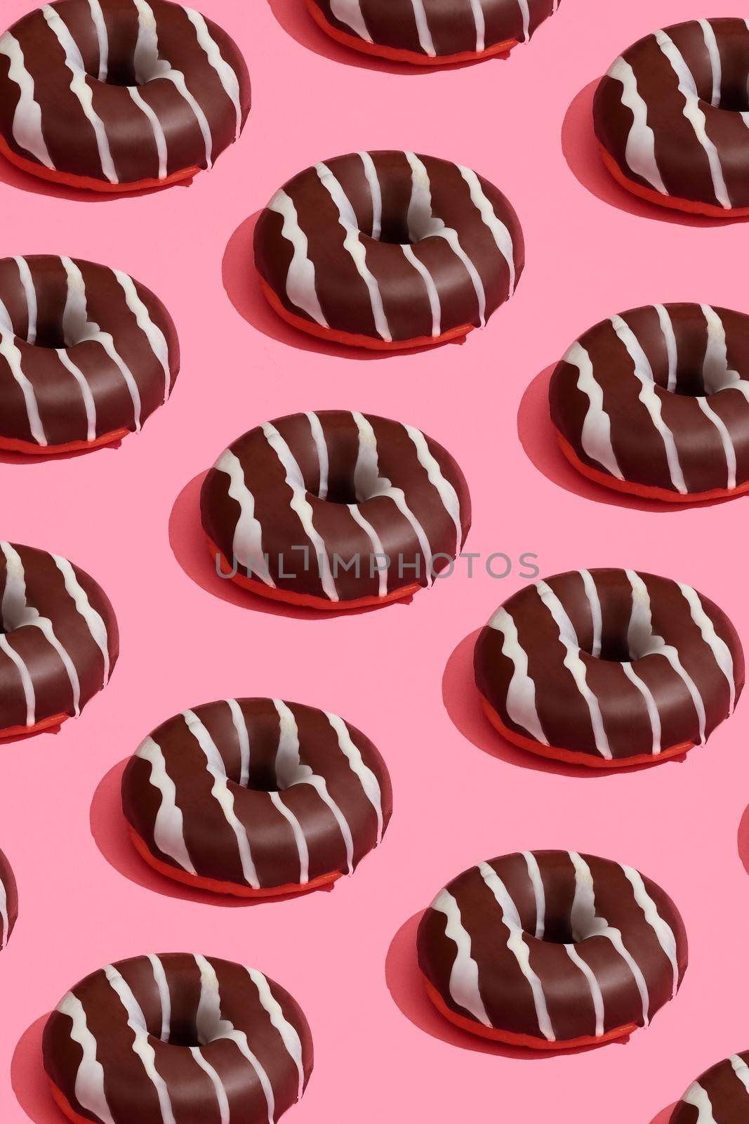 Concept food design with tasty chocolate glazed donut with white strips on coral pink pastel background top view pattern. Mock up, flat lay style