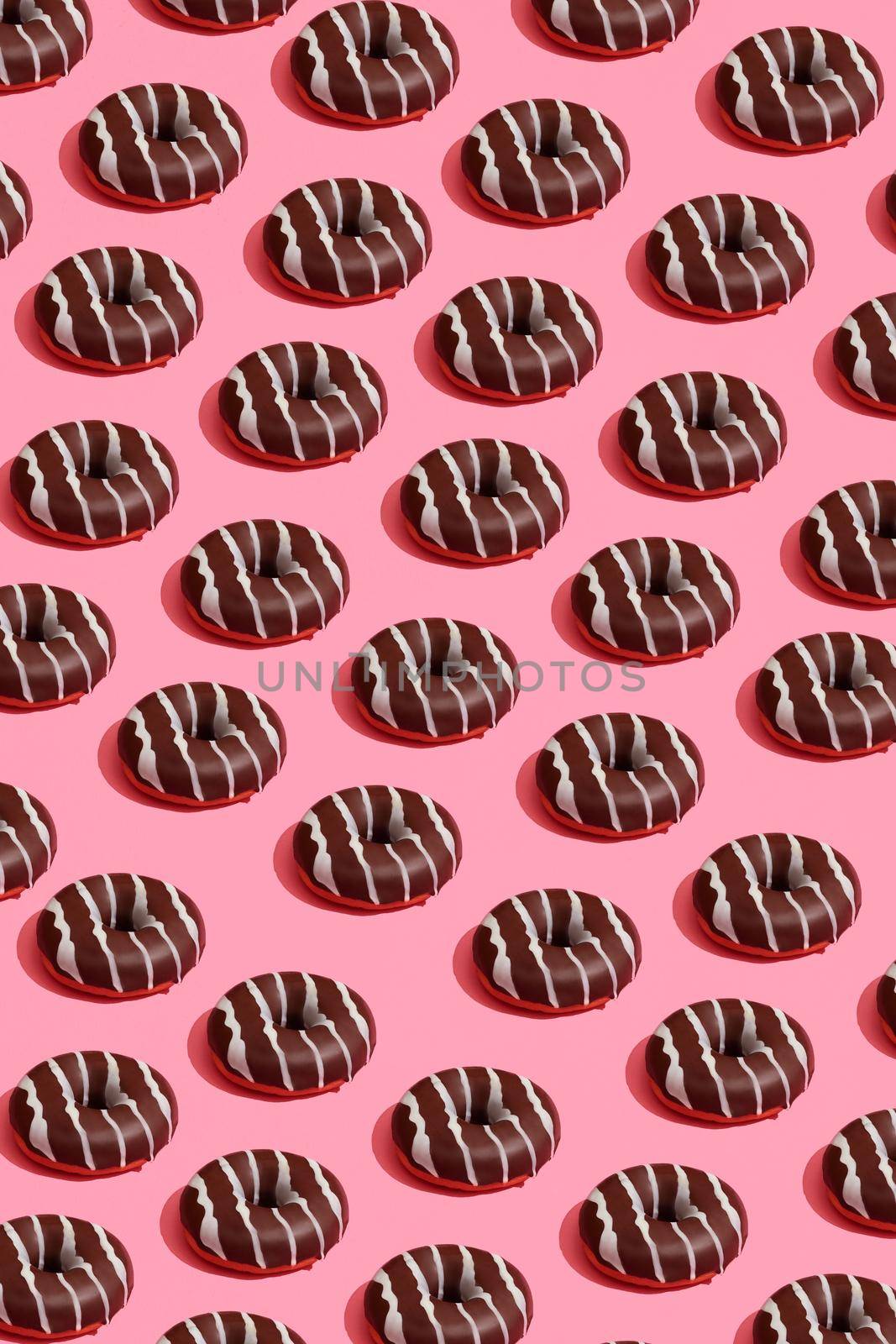 Concept food design with tasty chocolate glazed donut with white strips on coral pink pastel background top view pattern. Mock up, flat lay style