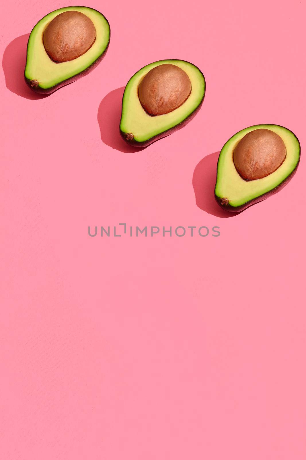 Colorful fruit pattern of fresh cutted avocado halves with pits on coral pink background, top view by nazarovsergey