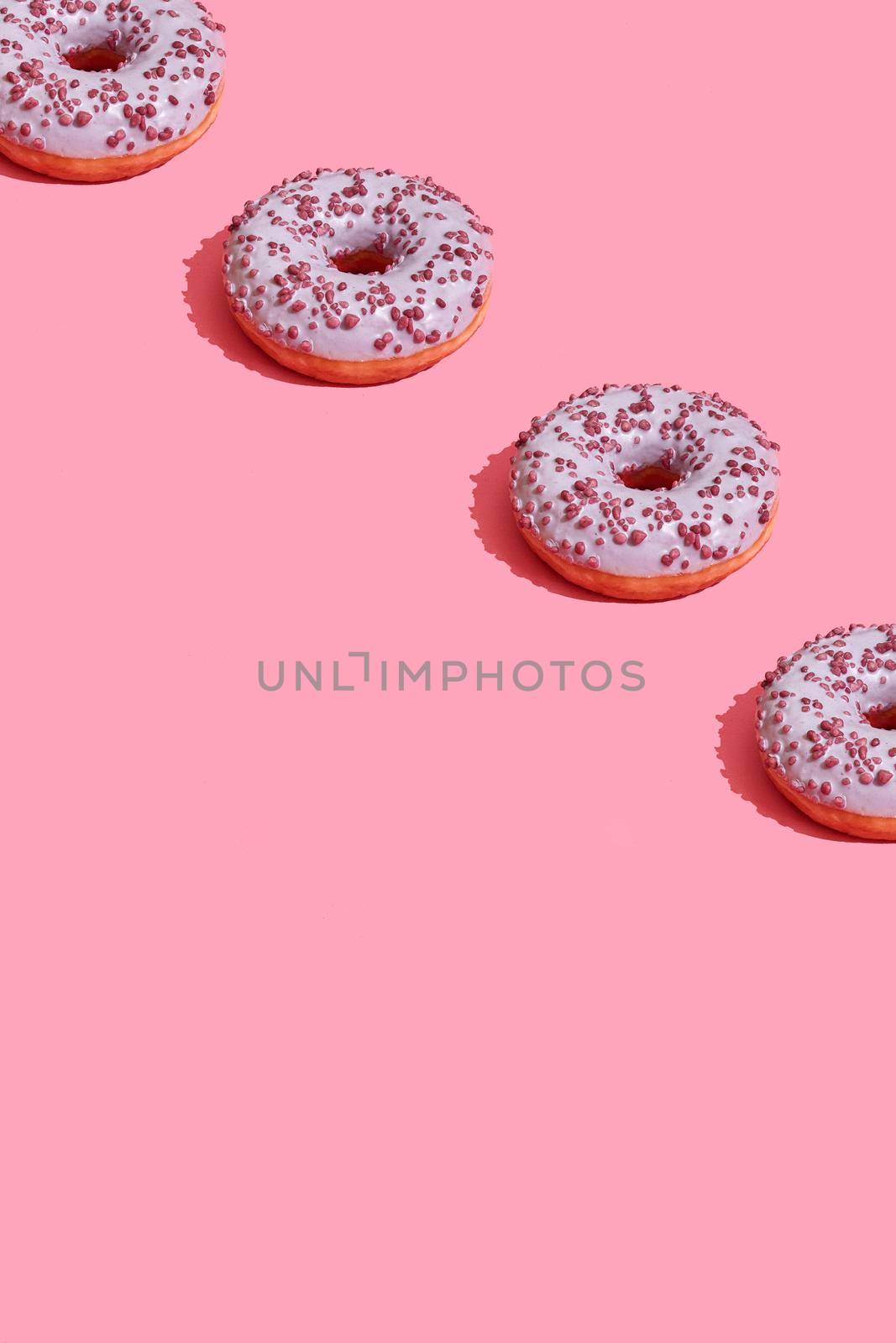 Concept food design with tasty pink glazed donut with red flakes on coral pink pastel background top view pattern. Mock up, flat lay style