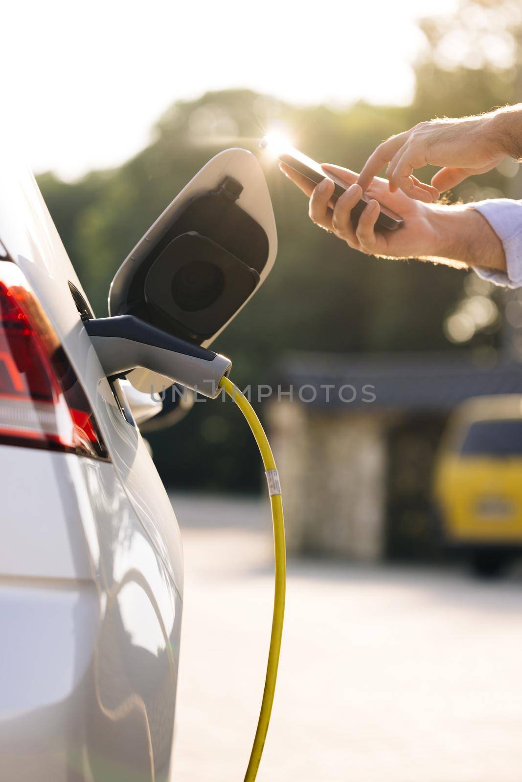 Businessman charging electric car at outdoor charging station Unrecognizable man unplugging electric car from charging station. Male unplugging in power cord to electric car using app on smartphone.
