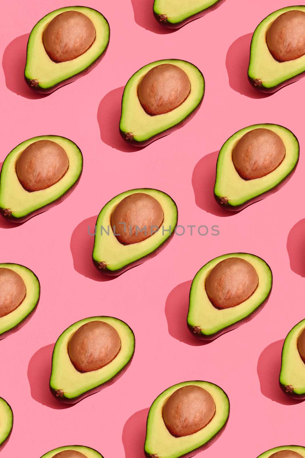 Food design. Top view of colorful fruit pattern of fresh cutted avocado halves with pits inside on coral pink pastel background. Mock up, flat lay style.