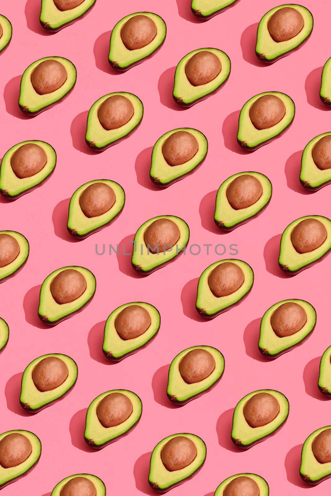 Colorful fruit pattern of fresh cutted avocado halves with pits on coral pink background, top view by nazarovsergey