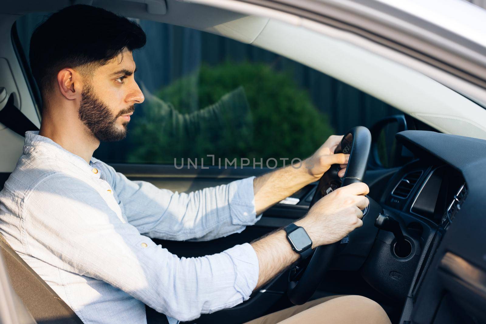 Businessman holding steering wheel while driving modern electric car on the street road. Confident man driving expensive car. Driver Turning Steering Wheel In Luxurious Auto On Trip by uflypro