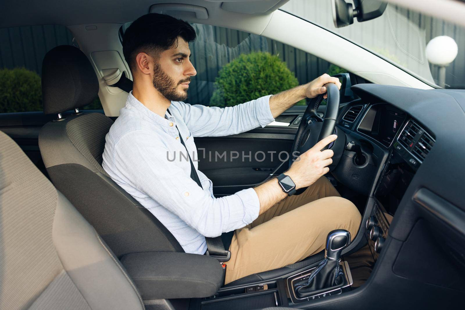 Confident man driving sitting in the car at sunset. Look around. Handsome bearded man driving electric car commuting to work. Automobile businessman traffic transportation work city.