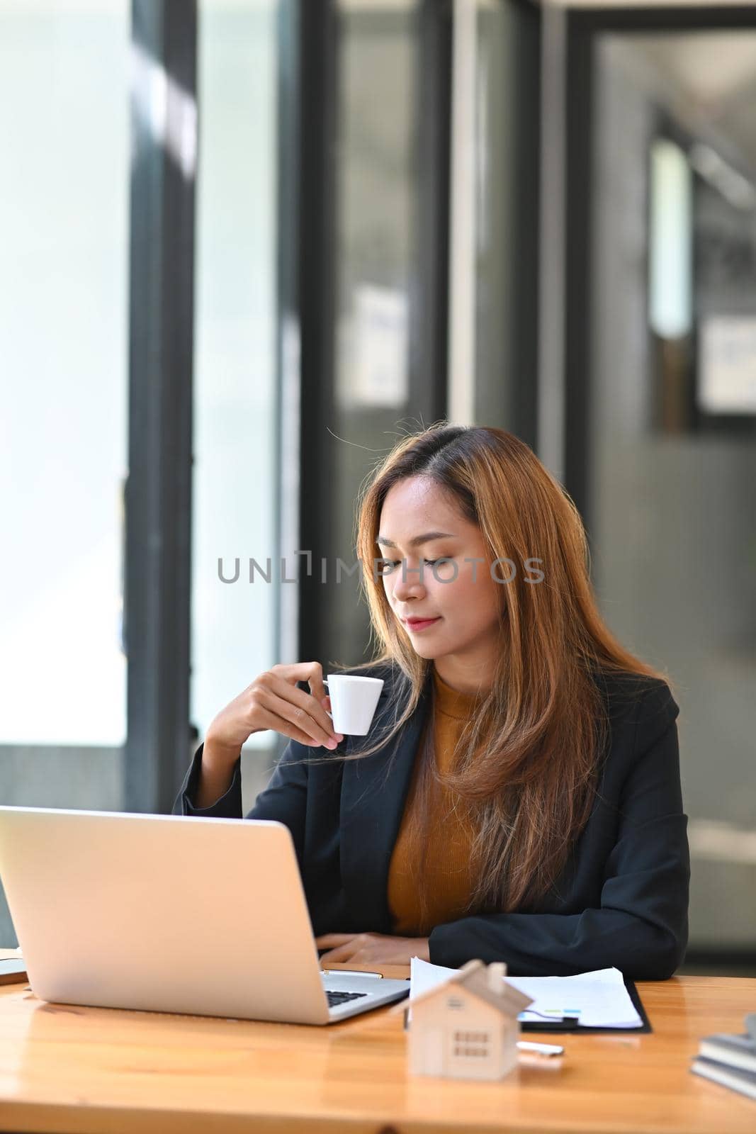 Portrait of confident businesswoman drinking coffee and working in modern office. by prathanchorruangsak