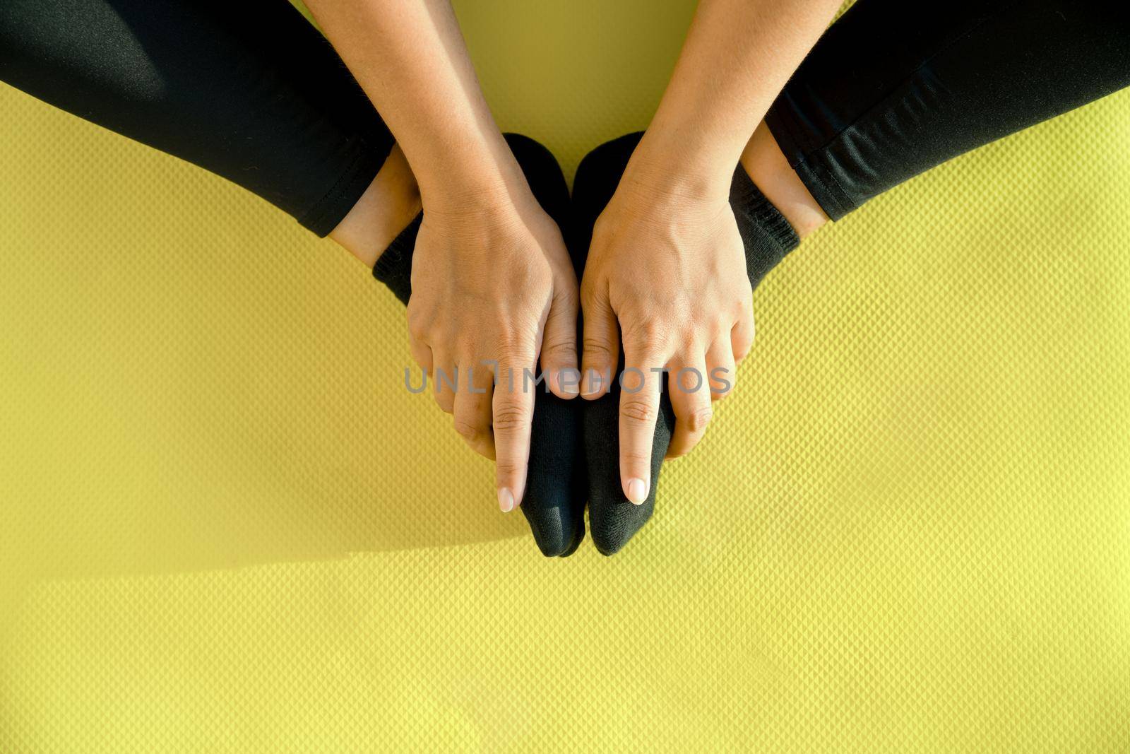 Girl does stretching on yoga mat, her legs are folded in butterfly pose and hands hold feet, close-up. Concept of healthy lifestyle. Copy space by Laguna781