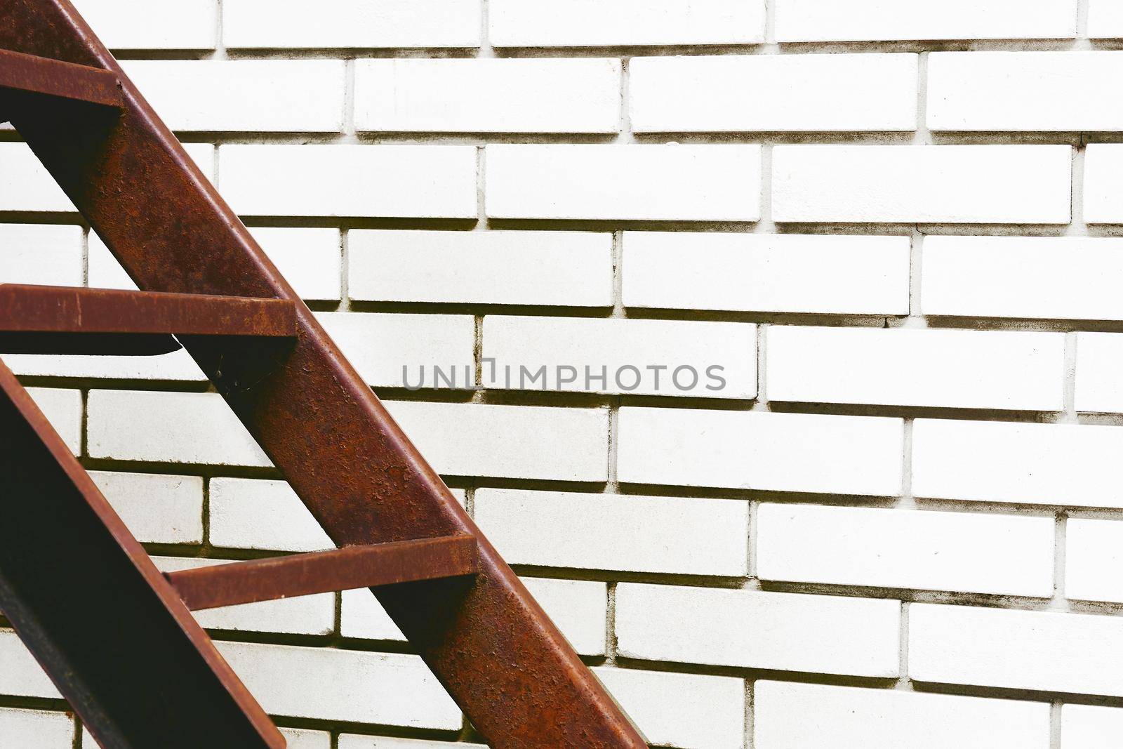 a structure consisting of a series of bars between two upright lengths of wood, metal used for climbing up or down.Part of the stairs red metal ladder leading up against of a white brick wall