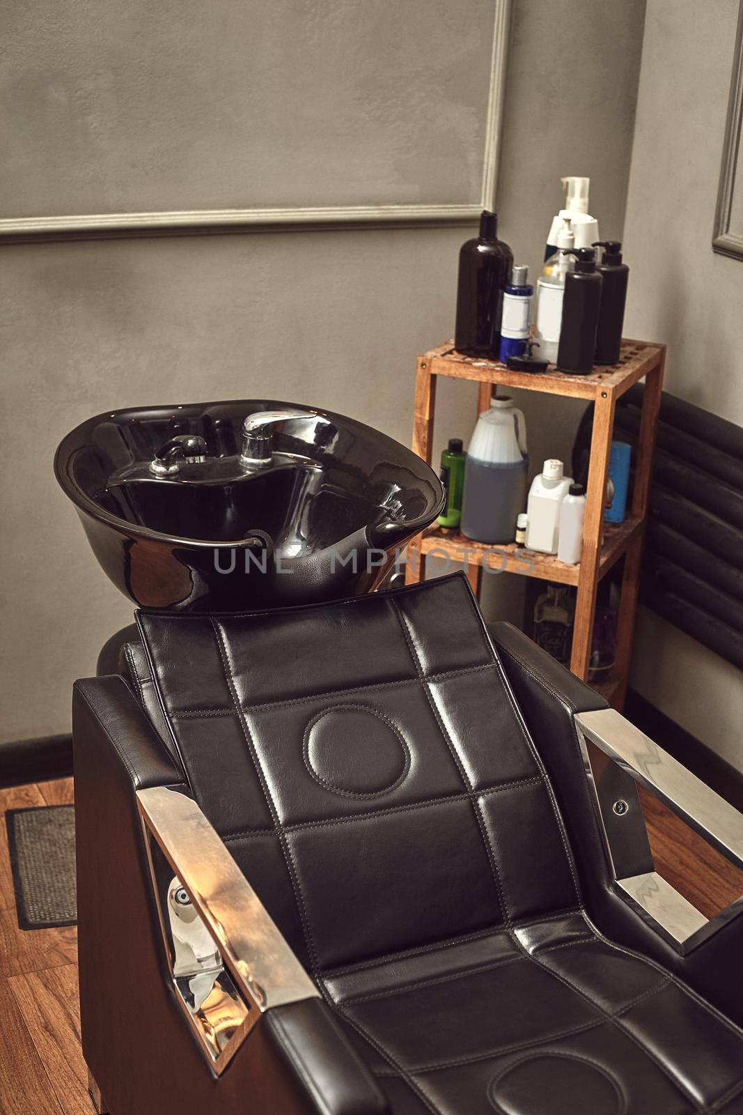 Black leather seat with wash basin in a barbershop interior with towels and shampoo on the side. by nazarovsergey